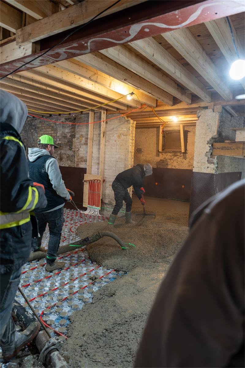 Crew placing and screeding concrete over radiant floor tubing in a basement