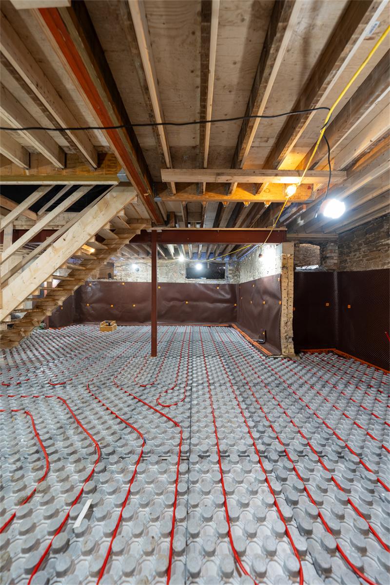 PEX radiant heating tubing laid across insulated panels on a basement sub-floor, ready to pour