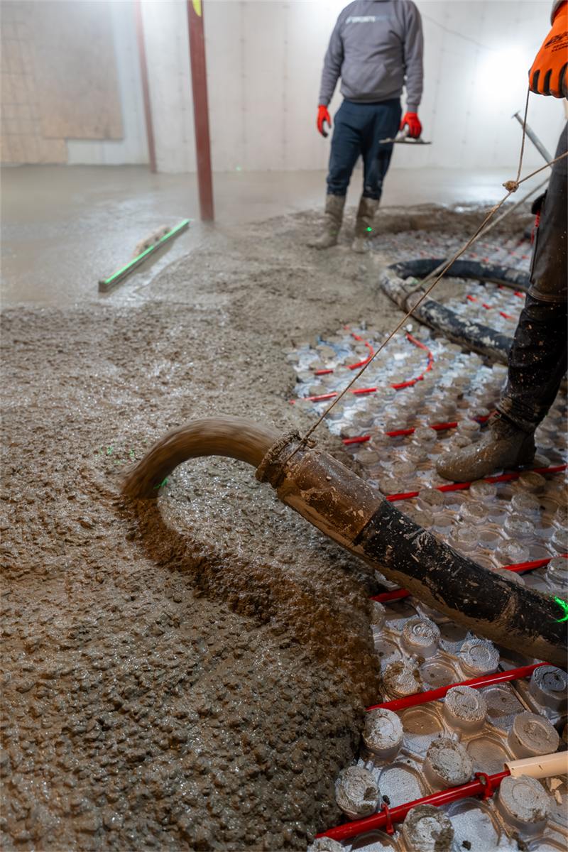 Worker screeding fresh concrete across insulation panels in a basement