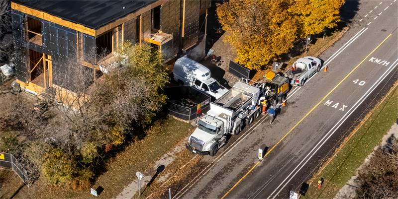 Aerial view of a concrete mixer and pump set up on a residential street beside a framed job site
