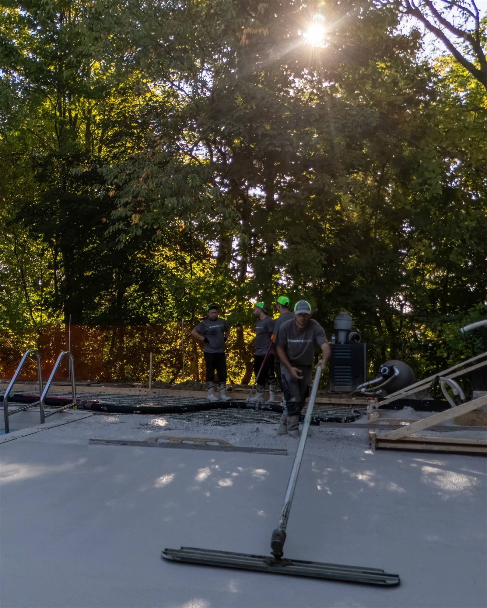 Crew pulling a screed bar across a fresh concrete slab in late afternoon sun
