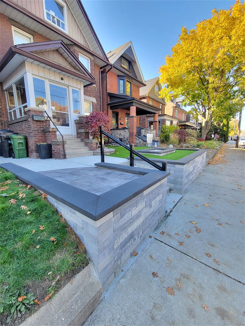Stone-veneer retaining wall with capstone and black railing in front of a Toronto row house