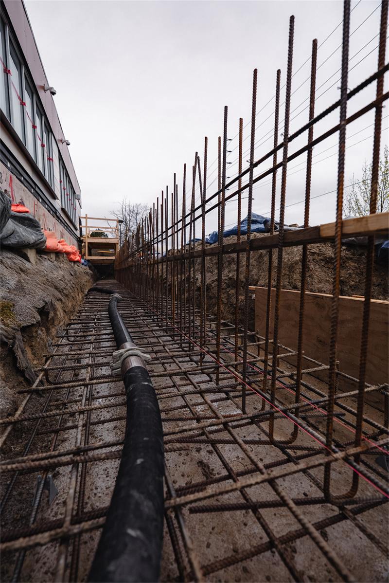 Excavated trench with rebar dowels along an existing foundation wall, prepared for an underpinning pour