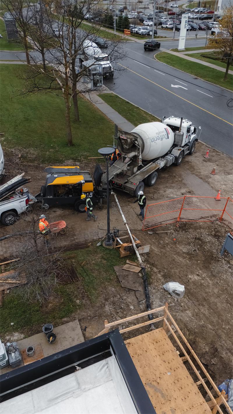 Aerial view of a mixer truck feeding a trailer-mounted line pump, with the hose run up to a framed structure above