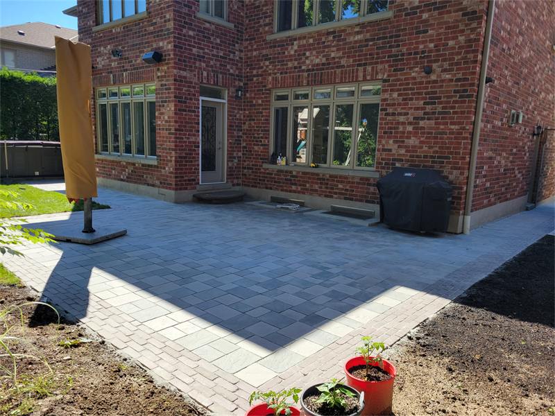 Paver patio behind a brick house with a freshly cut garden edge