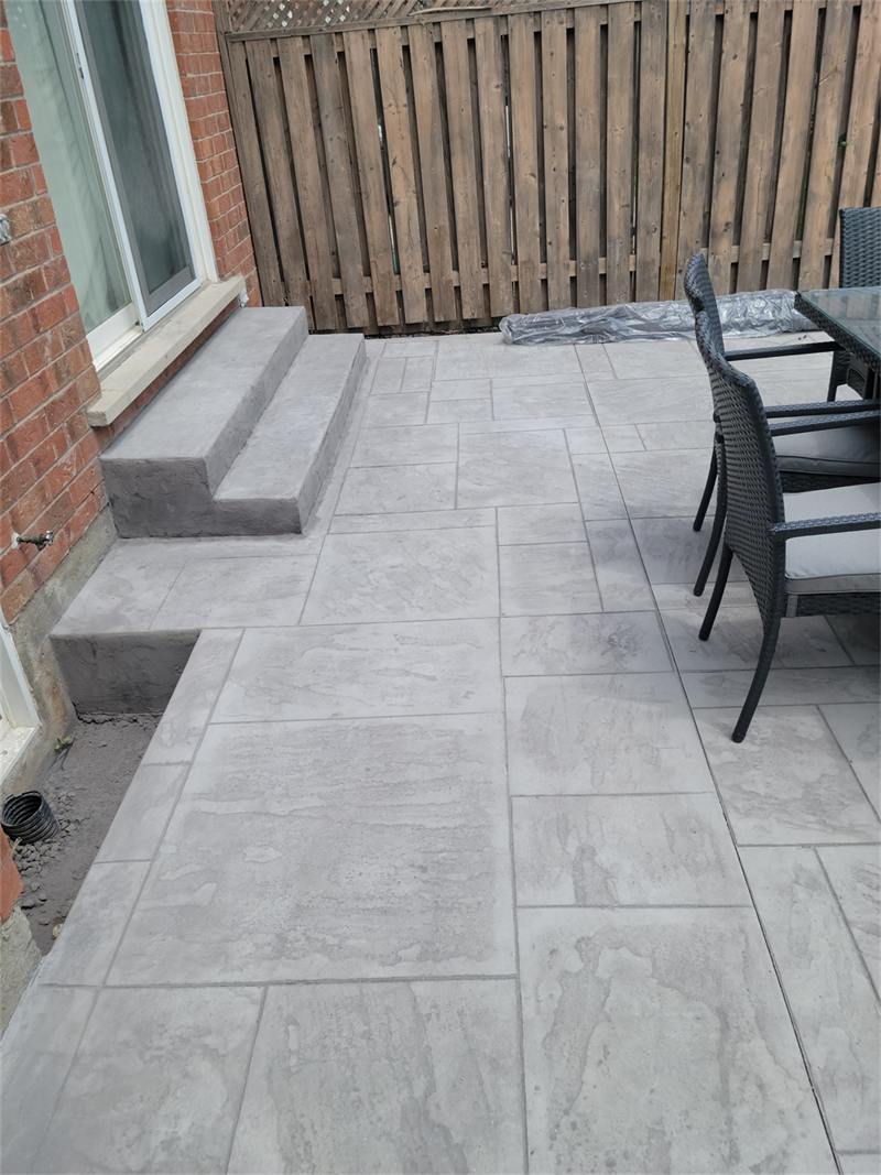Grey large-format slab patio with outdoor chairs against a wood fence