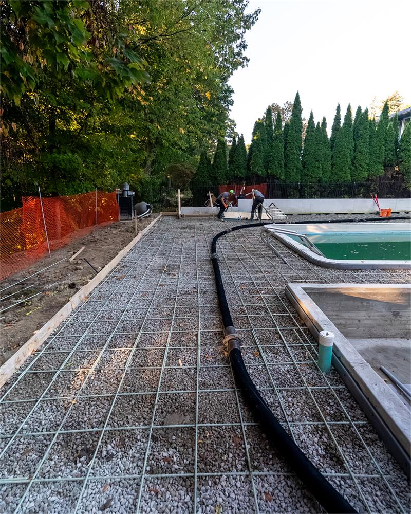 Reinforcing mesh laid over a compacted gravel base around a swimming pool