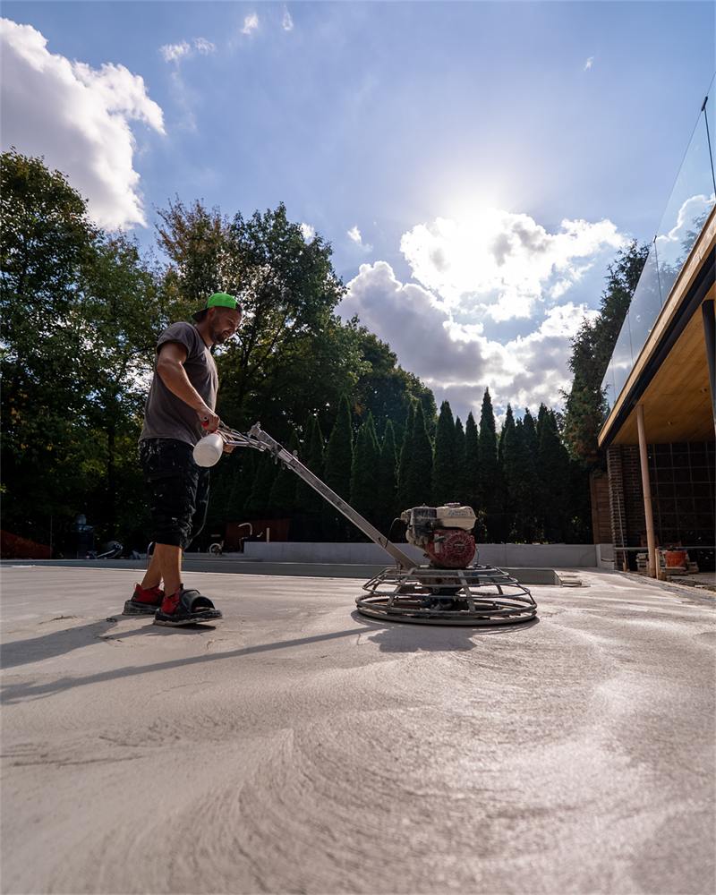 Worker power-trowelling a pool deck slab in full sun