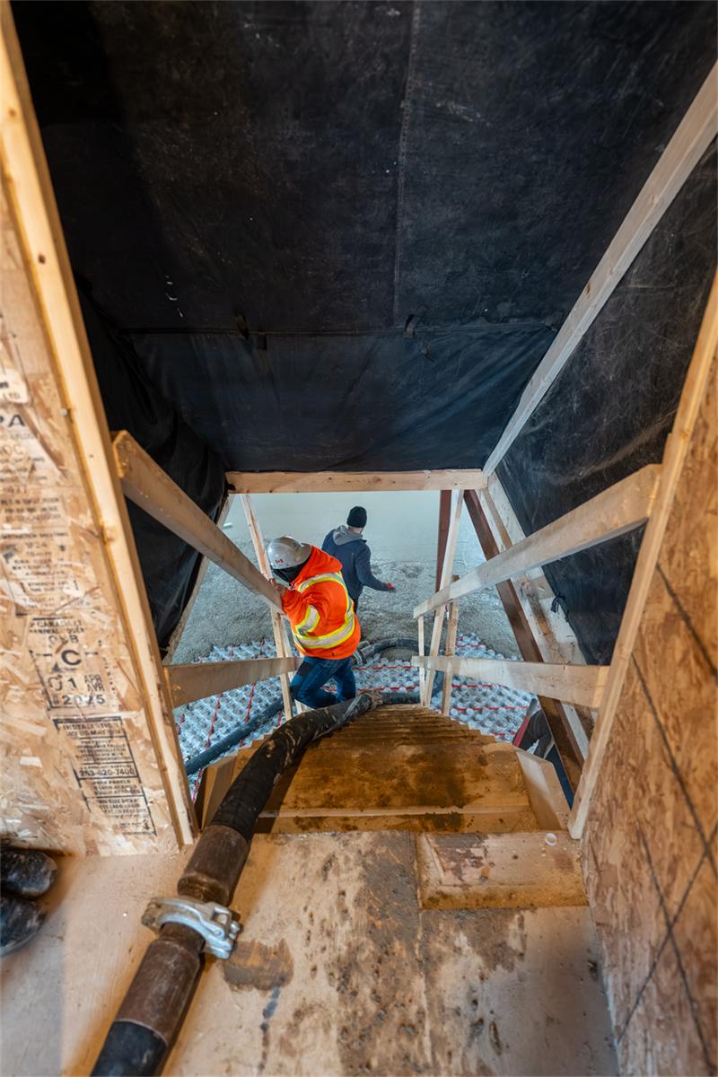 Pump hose fed down into a basement mid-pour, with the new floor's reinforcement laid out below