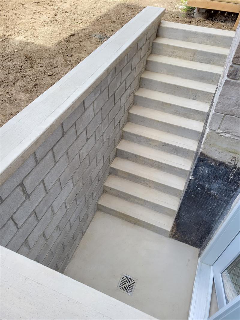 Finished concrete basement walkout stairwell with block retaining walls and a floor drain