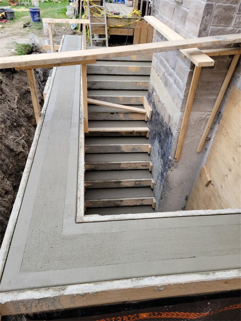 Black waterproofing membrane applied to a foundation wall beside a newly formed basement stairwell
