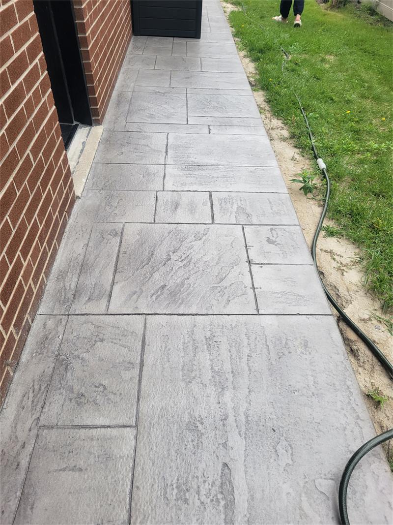 Large-format stamped concrete walkway running along a brick house