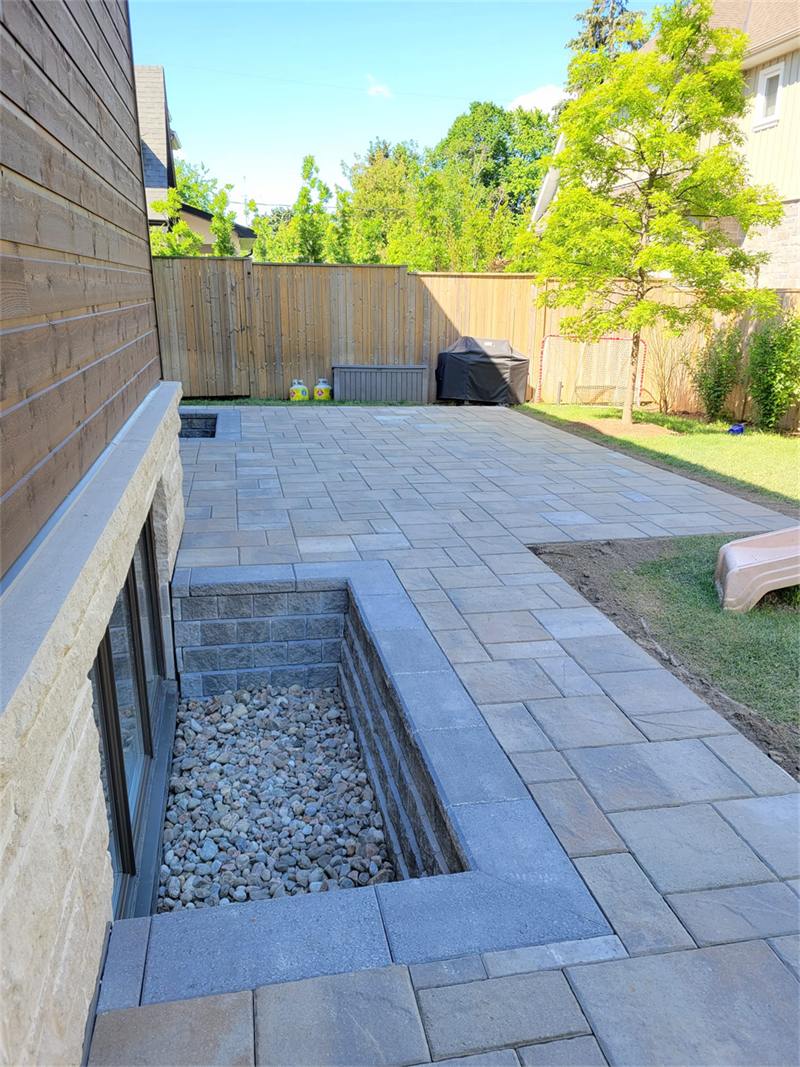 Window well built into a paver patio, finished flush with the surrounding hardscape